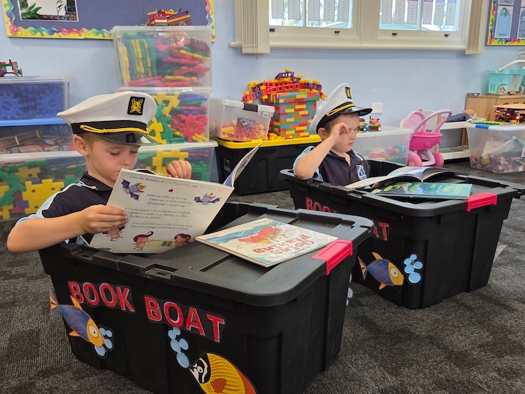 Two students reading is a book boats. A large tub made into a boat.